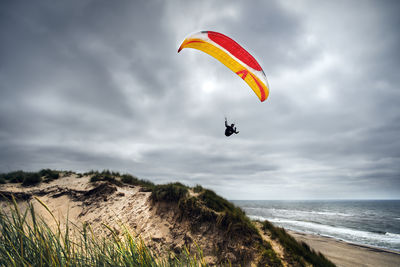 Person paragliding over sea against sky