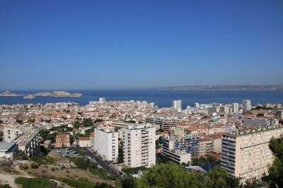 High angle view of townscape by sea against clear blue sky