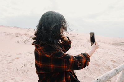 Rear view of woman standing at beach against sky