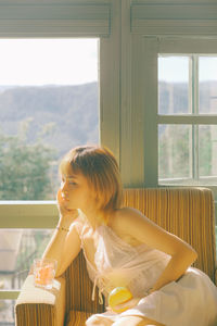 Woman looking away while sitting in chair at home