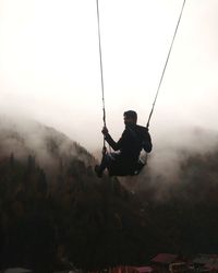 Man swinging against sky