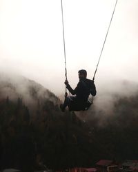 Man on swing at playground against sky