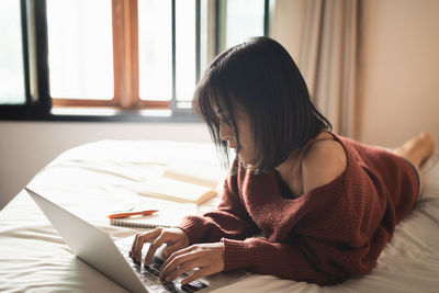 Rear view of girl using laptop on bed