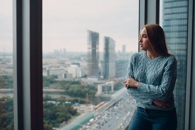 Young woman looking through glass window in city