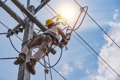 Low angle view of man working on rope against sky