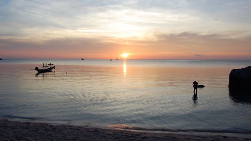 Silhouette person and boat in sea against cloudy sky during sunset