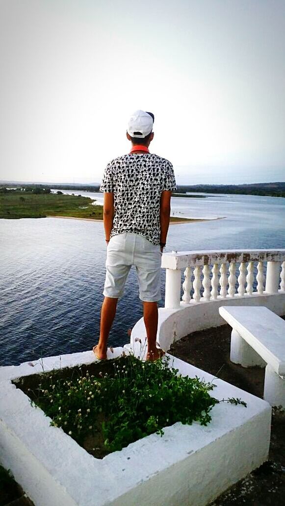 REAR VIEW OF MAN STANDING BY SEA AGAINST SKY