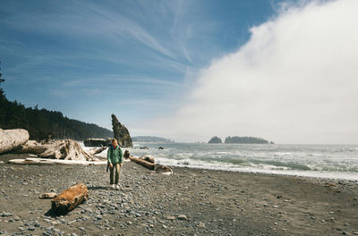 Hiker walking on shore at beach against sky at olympic national park