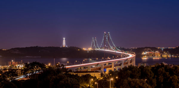 Illuminated 25 de abril bridge over tagus river by christ the king against sky at night