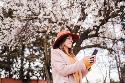 Low angle view of woman wearing hat against cherry blossom