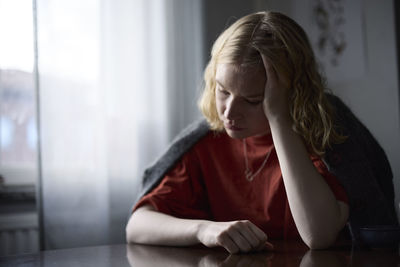 Pensive teenage girl sitting at table with head in hands