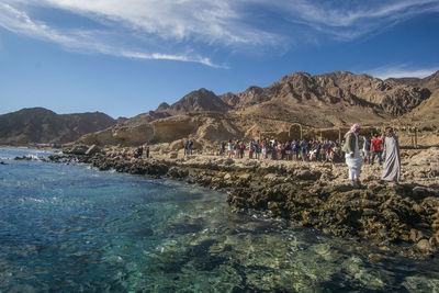 Group of people on rock by mountains against sky