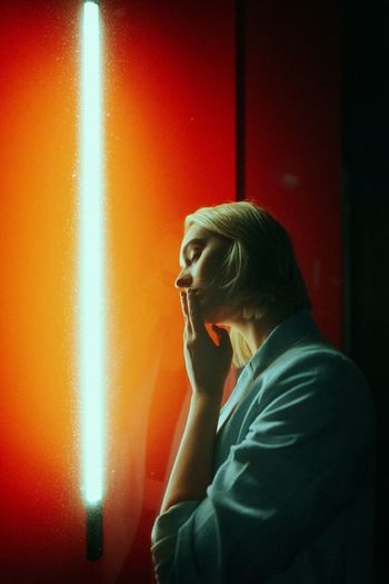 WOMAN LOOKING AWAY WHILE STANDING AGAINST WALL