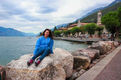 Portrait of woman sitting on rock by lake against sky