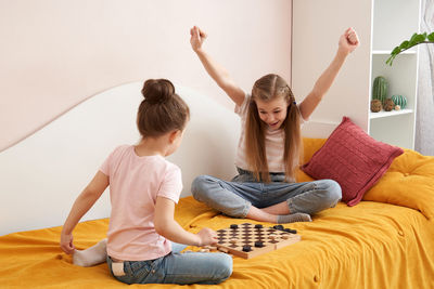 Sisters playing draughts board game on bed