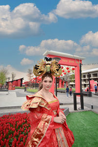 Woman standing by red traditional building against cloudy sky