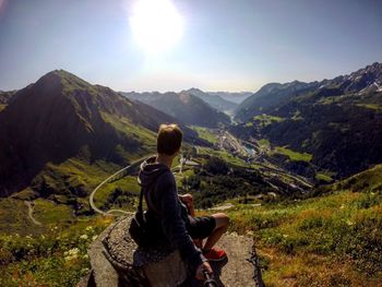 Side view of man sitting on rock at gotthard pass against sky
