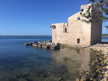 Building by sea against clear blue sky