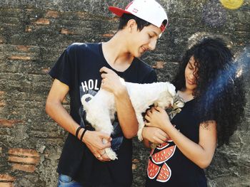Teenage couple with dog and kitten standing against wall