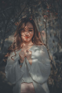 Portrait of young woman standing against tree