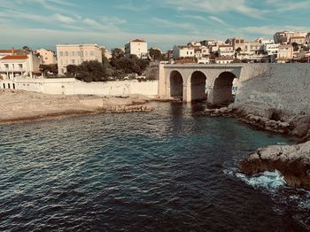 Arch bridge over river by buildings in city against sky