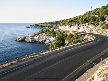 Scenic view of road by sea against clear sky