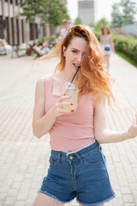 Cheerful young woman drinking juice on footpath