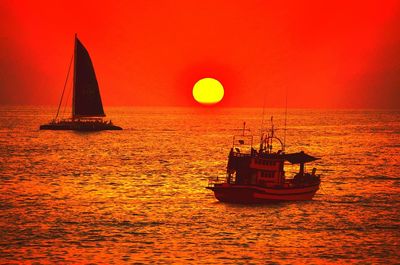 Boats sailing in sea at sunset