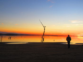 Silhouette man standing on beach against sky during sunset