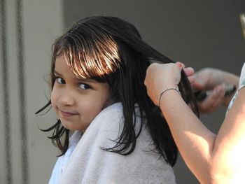 Cropped image of hairdresser cutting girl hair in salon