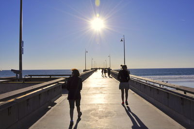 People walking on pier over sea against clear sky during sunny day