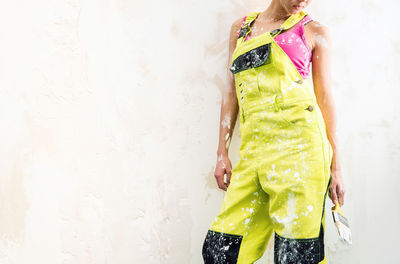 Midsection of female construction worker wearing coveralls while standing with paintbrush against wall