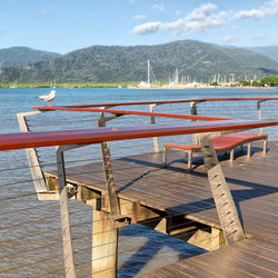 Empty chairs and tables by lake against sky