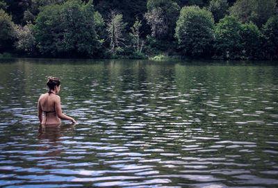 Rear view of woman standing in lake at forest