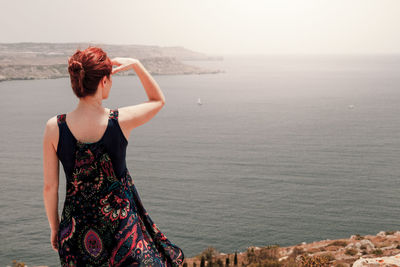 Rear view of woman standing on cliff against sea