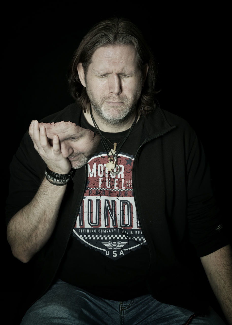 PORTRAIT OF MAN SITTING ON BLACK BACKGROUND