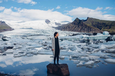 Woman standing on rock by lake against sky