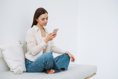 Beautiful smiling woman teenager girl with dark long hair in white shirt using mobile phone in hand 