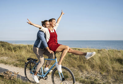 Young woman riding bicycle by sea against sky