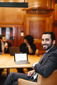 Portrait of smiling bearded male financial advisor sitting at conference table in board room