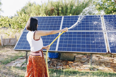 Woman spraying water and cleaning solar panels in garden