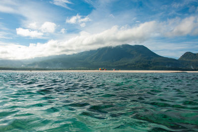 Scenic view of sea by mountain against sky