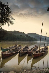 Boats moored in lake against sky during sunset