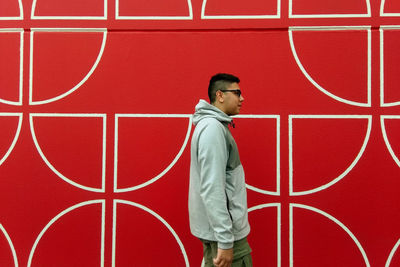 Side view of young man walking by red wall