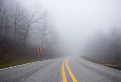 Road amidst trees against sky during foggy weather