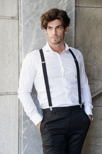 Man wearing suspenders while standing by wall