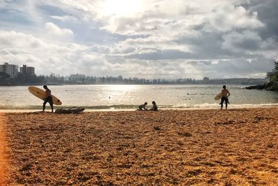 People with surfboard at beach against sky