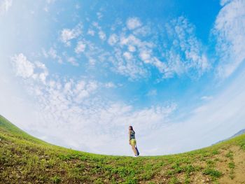 Low angle view of woman standing on field against blue sky