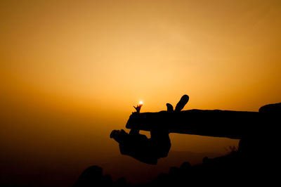 Silhouette man doing stunt on rock against sky during sunset