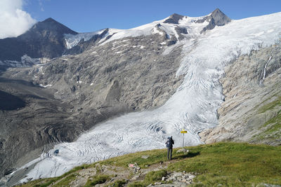 Rear view of man standing by snowcapped mountains against sky